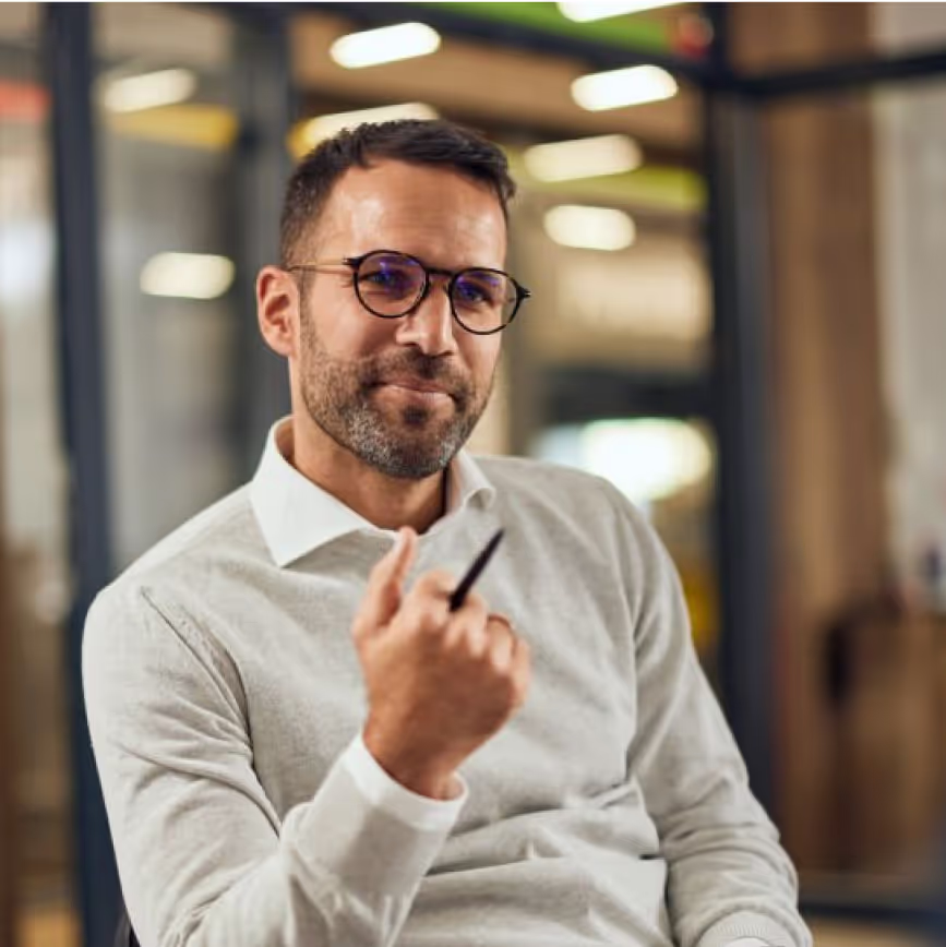 Professional wearing glasses and a light sweater in an office setting, looking confidently at camera