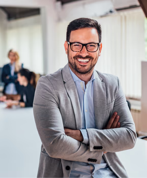 Professional in grey suit jacket and glasses smiling confidently in bright office environment